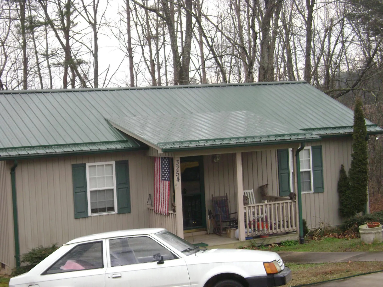 Green metal roof and front porch on a tan sided cottage in Belmont
